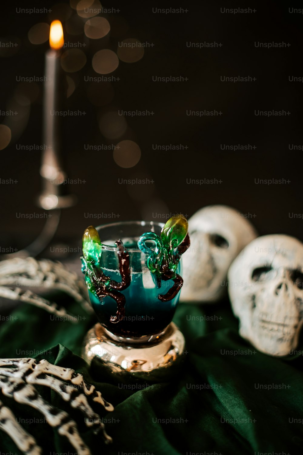 a glass with a green liquid in it next to two skulls