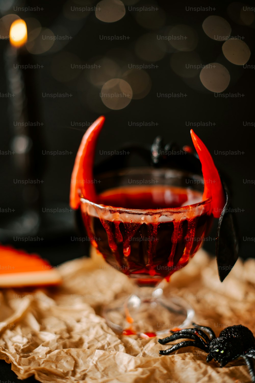 a glass of red liquid with a devil's head sticking out of it