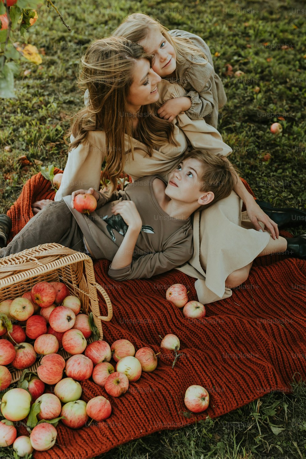 a woman and two children laying on a blanket with apples