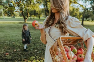 a woman holding a basket of apples next to a little girl