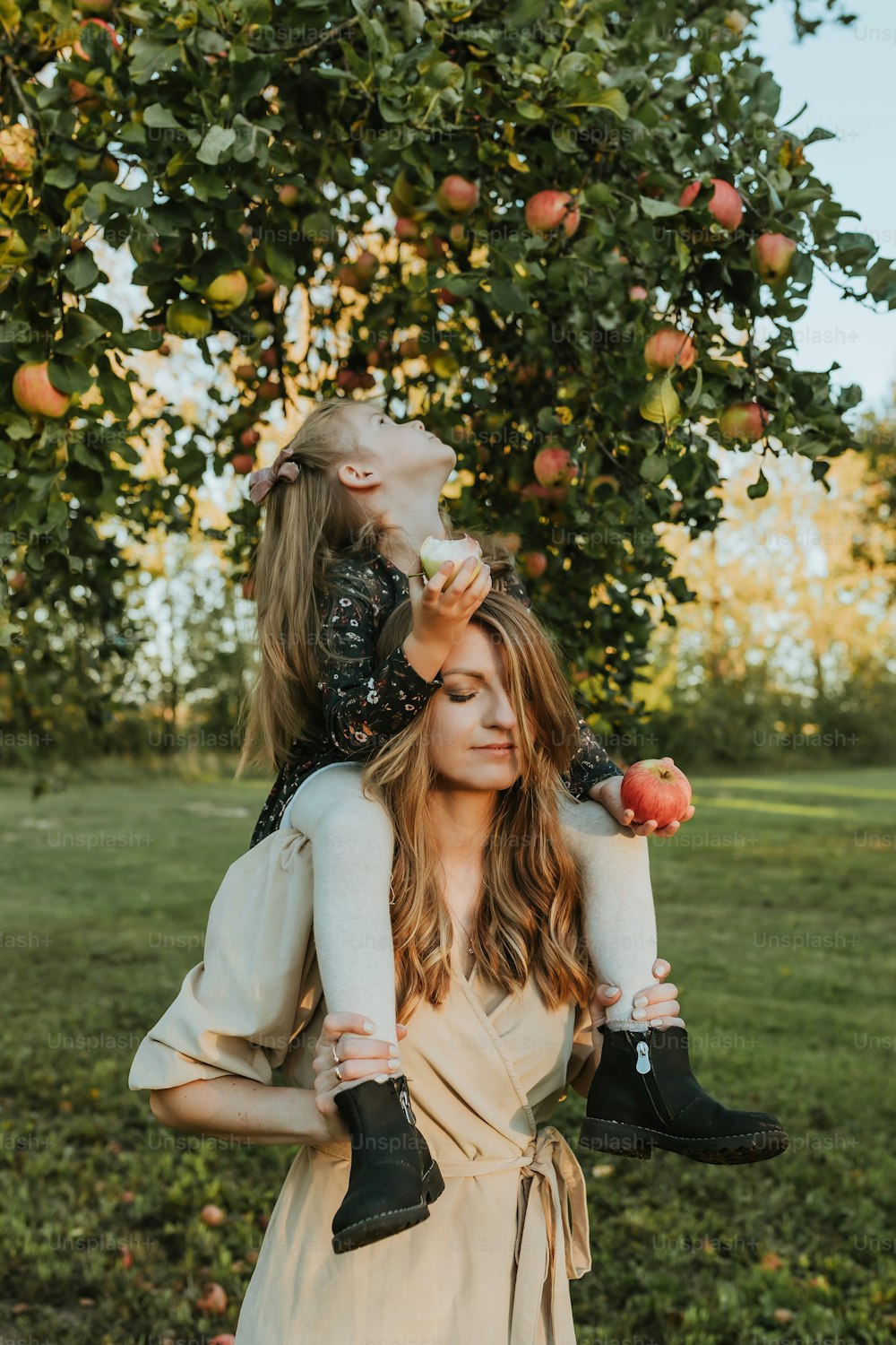 a woman holding a child in her arms under an apple tree