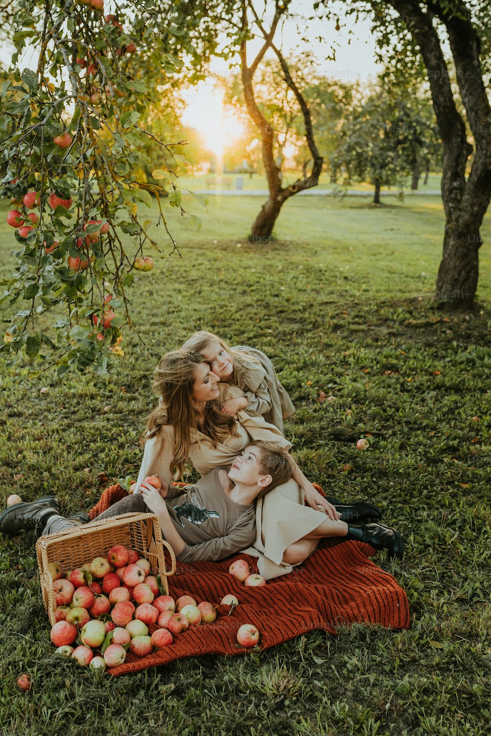 a mother and her two children sitting under an apple tree