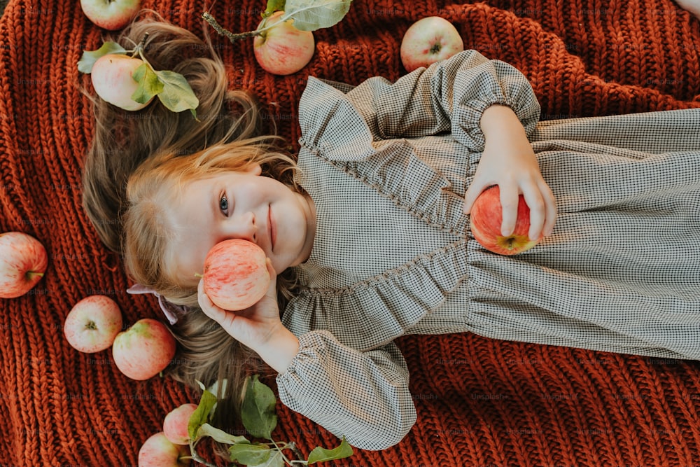 Une petite fille allongée sur une couverture avec des pommes