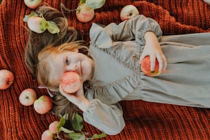 a little girl laying on a blanket with apples