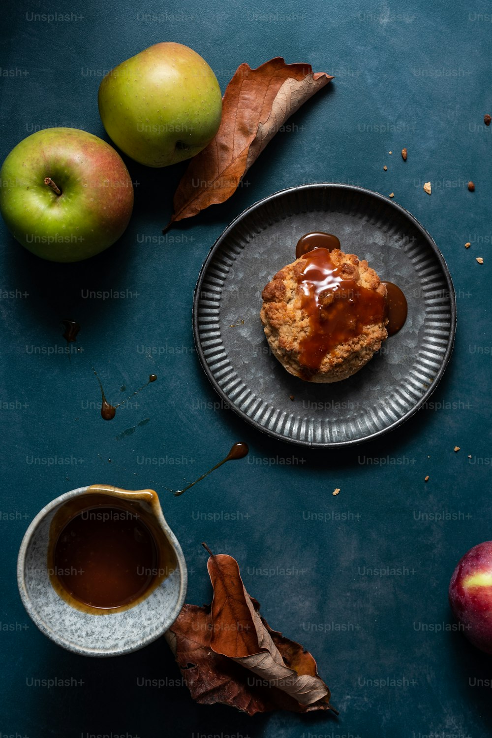 un panecillo en un plato junto a dos manzanas y una taza de café