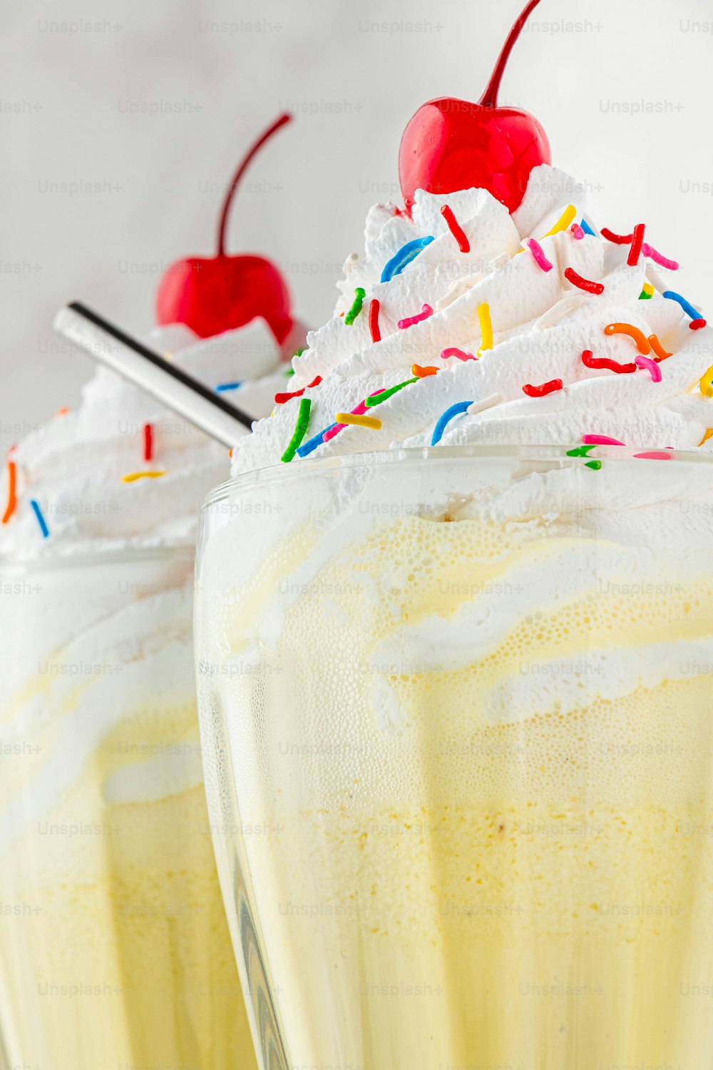 two glasses filled with yellow liquid and topped with whipped cream and sprinkles