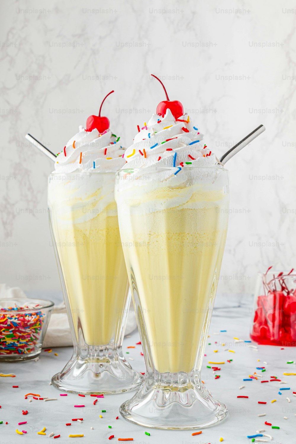 two glasses filled with yellow liquid and topped with whipped cream and sprinkles