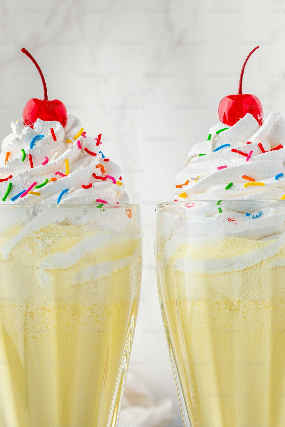 a couple of glasses filled with yellow liquid and topped with whipped cream and sprin