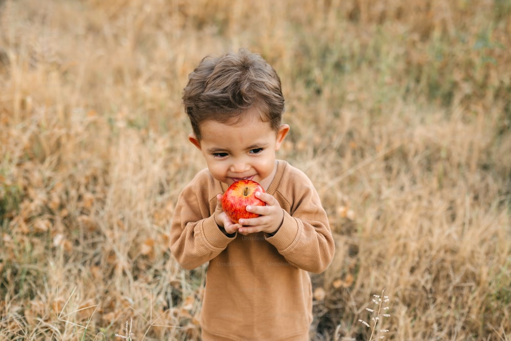 a young boy holding an apple in a field
