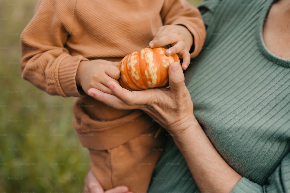 a woman holding a baby who is holding a pumpkin