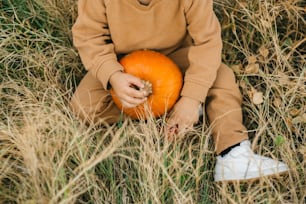 a little boy sitting in a field holding a pumpkin