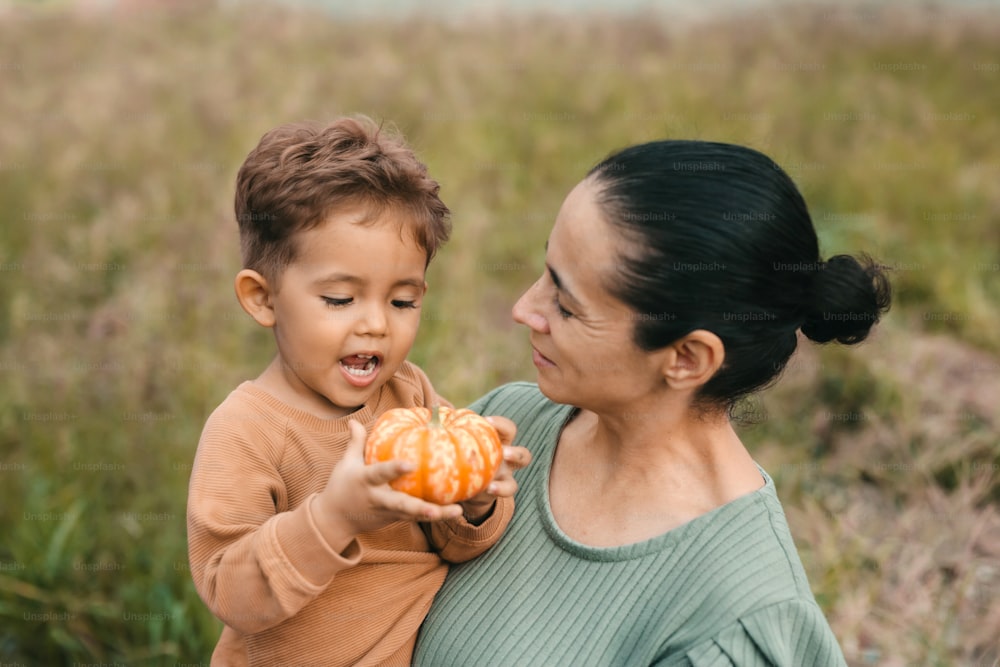 a woman holding a small child holding a pumpkin