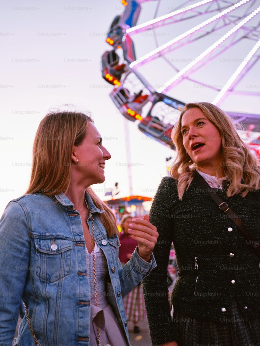 two women standing next to each other in front of a ferris wheel