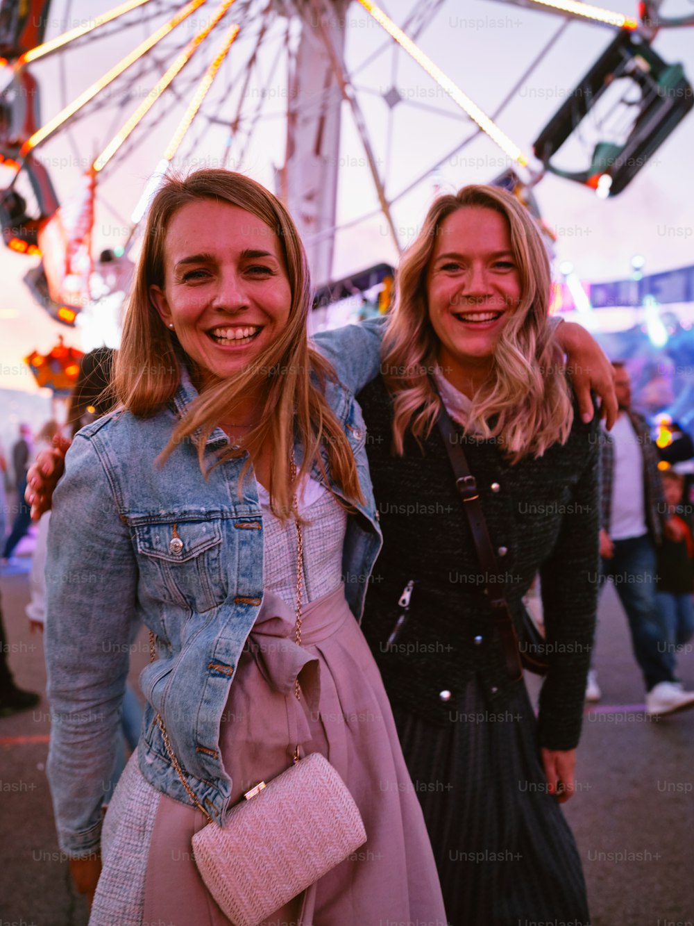 two women standing next to each other in front of a ferris wheel