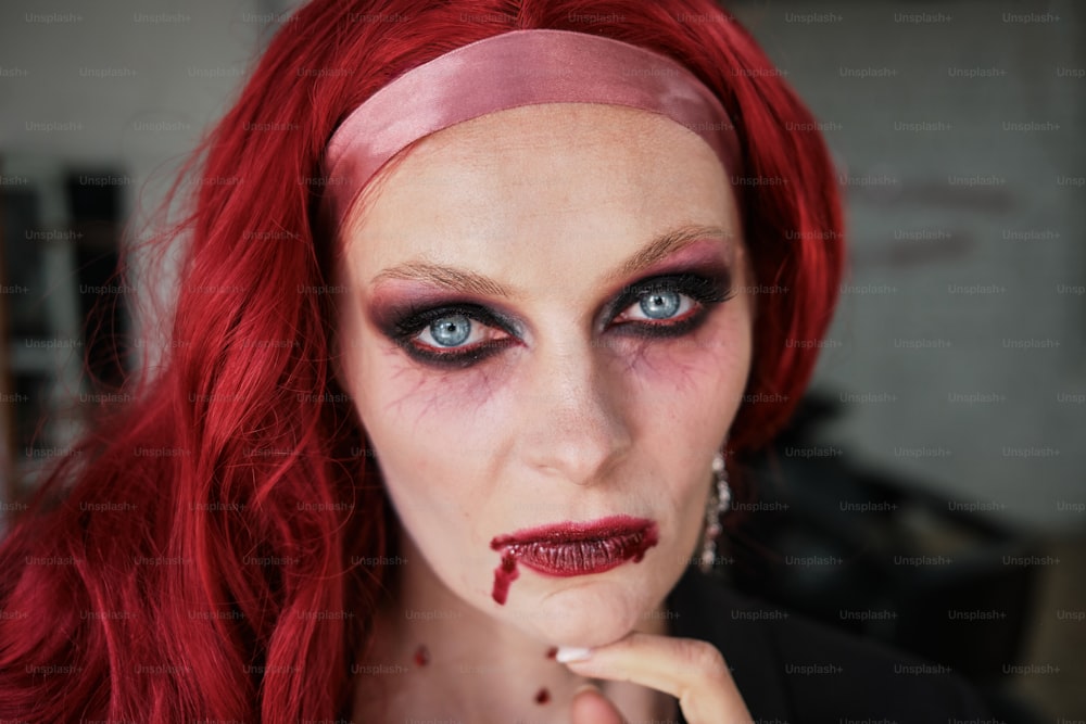 Uma mulher com cabelos ruivos e maquiagem tem sangue no rosto