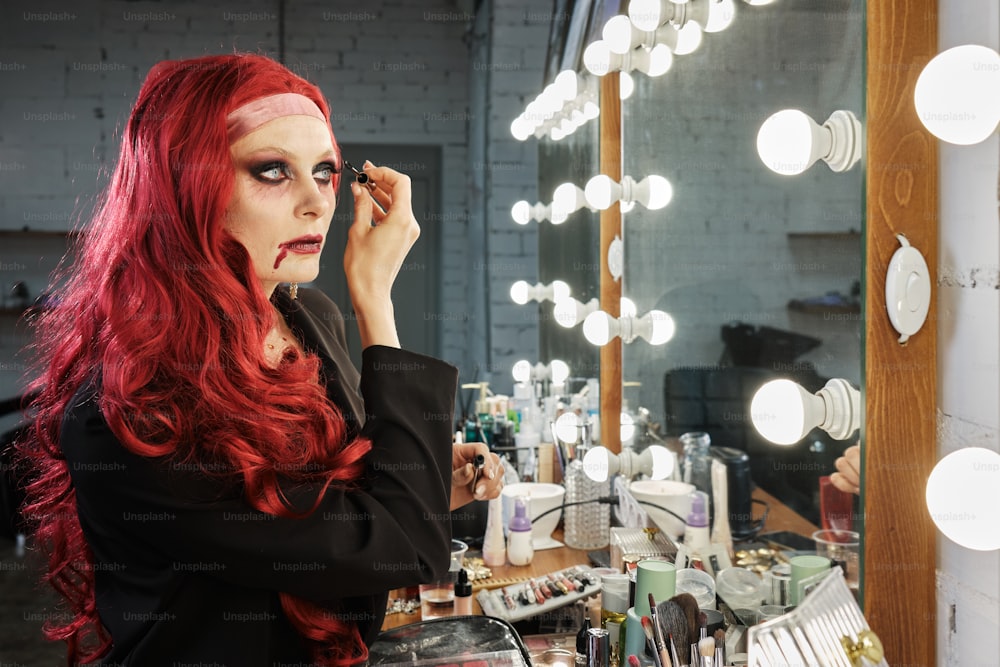 a woman with red hair is doing makeup in front of a mirror