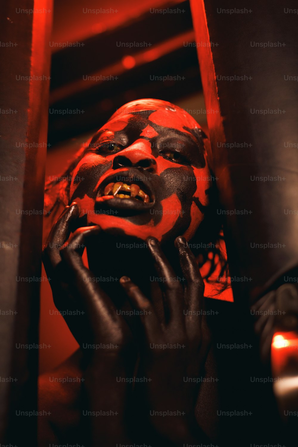 eine Person in einer rot-schwarzen Maske, die ihre Hand vor ihr Gesicht hält
