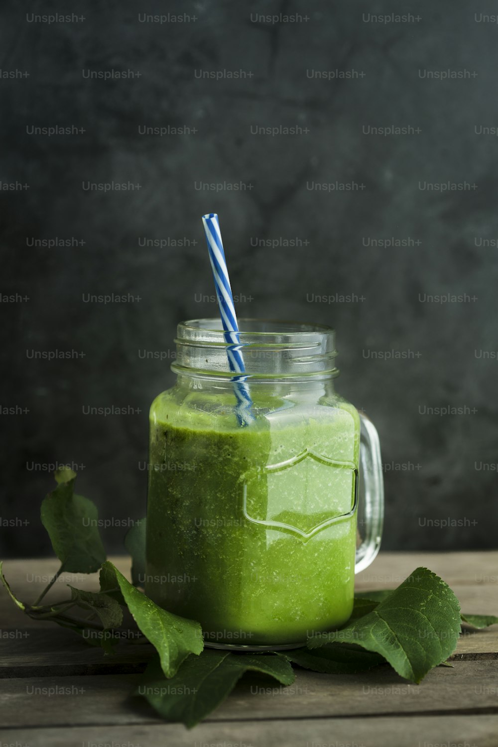 um smoothie verde em um frasco de pedreiro com um canudo listrado azul