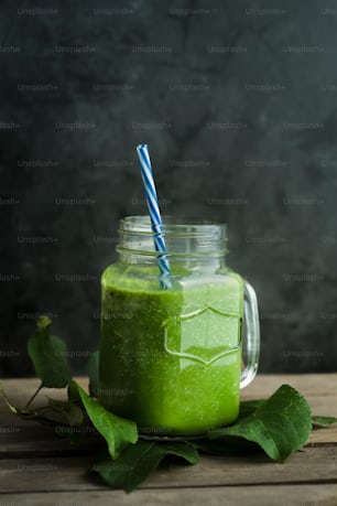 a green smoothie in a mason jar with a blue striped straw