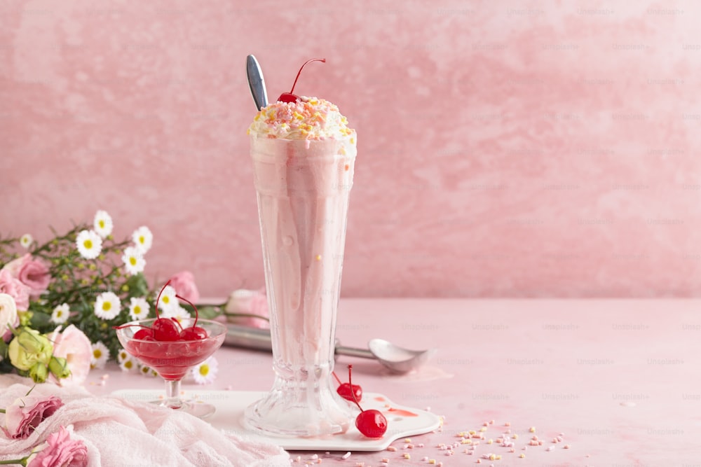 a pink smoothie in a tall glass with a cherry garnish on top
