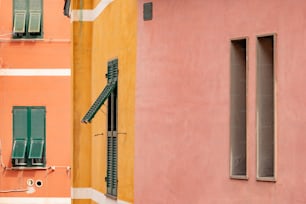 a pink building with green shutters next to a yellow building