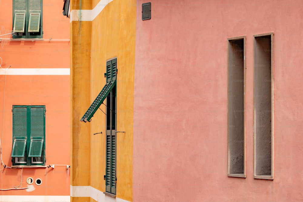 a pink building with green shutters next to a yellow building