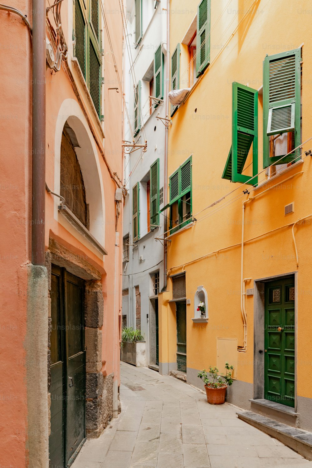 Un callejón estrecho con ventanas verdes con persianas y persianas verdes