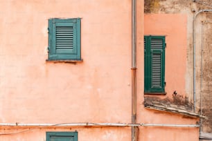 a pink building with green shutters and a clock