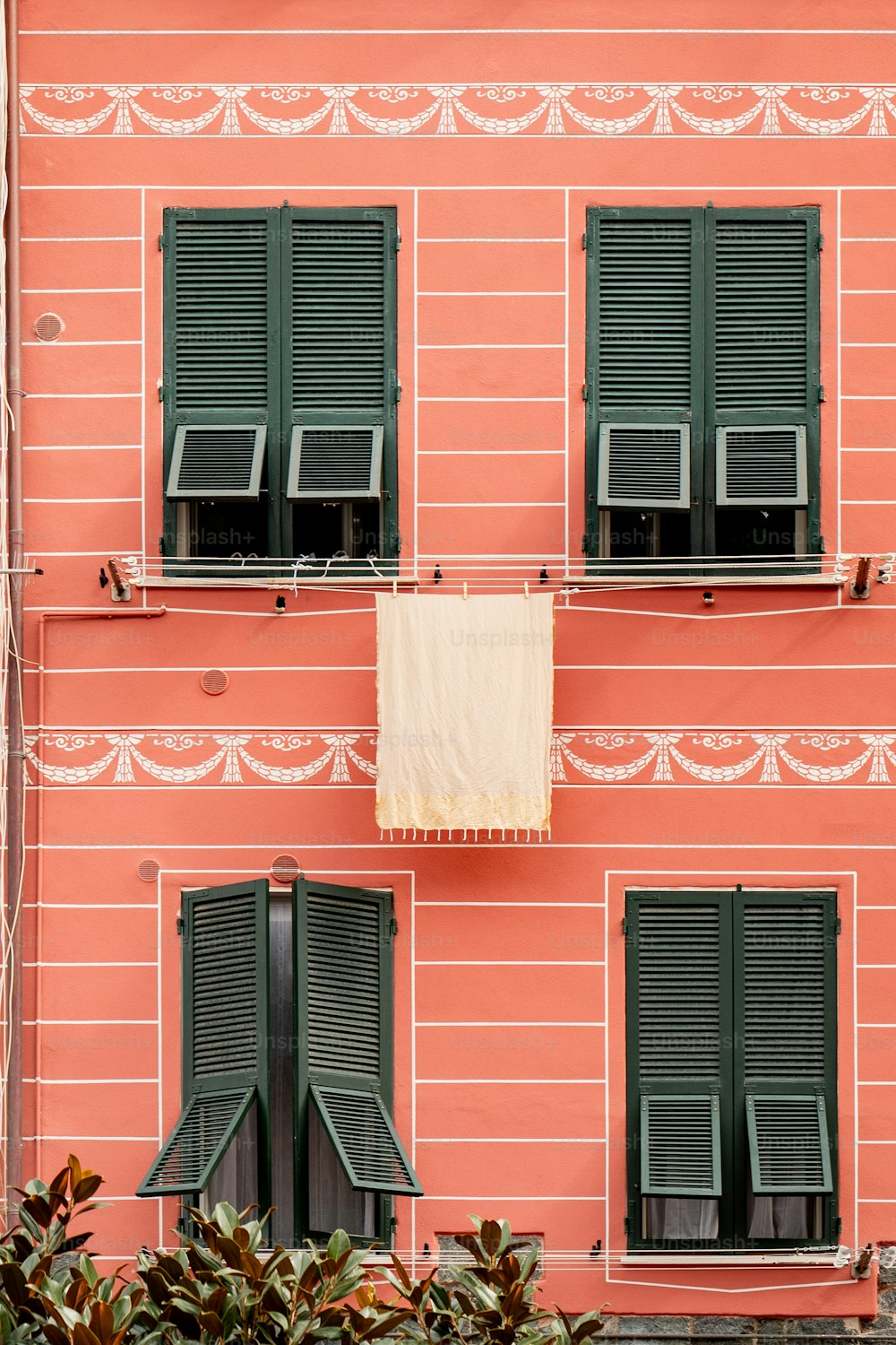 Ein rosafarbenes Gebäude mit grünen Fensterläden und einem Handtuch, das aus dem Fenster hängt