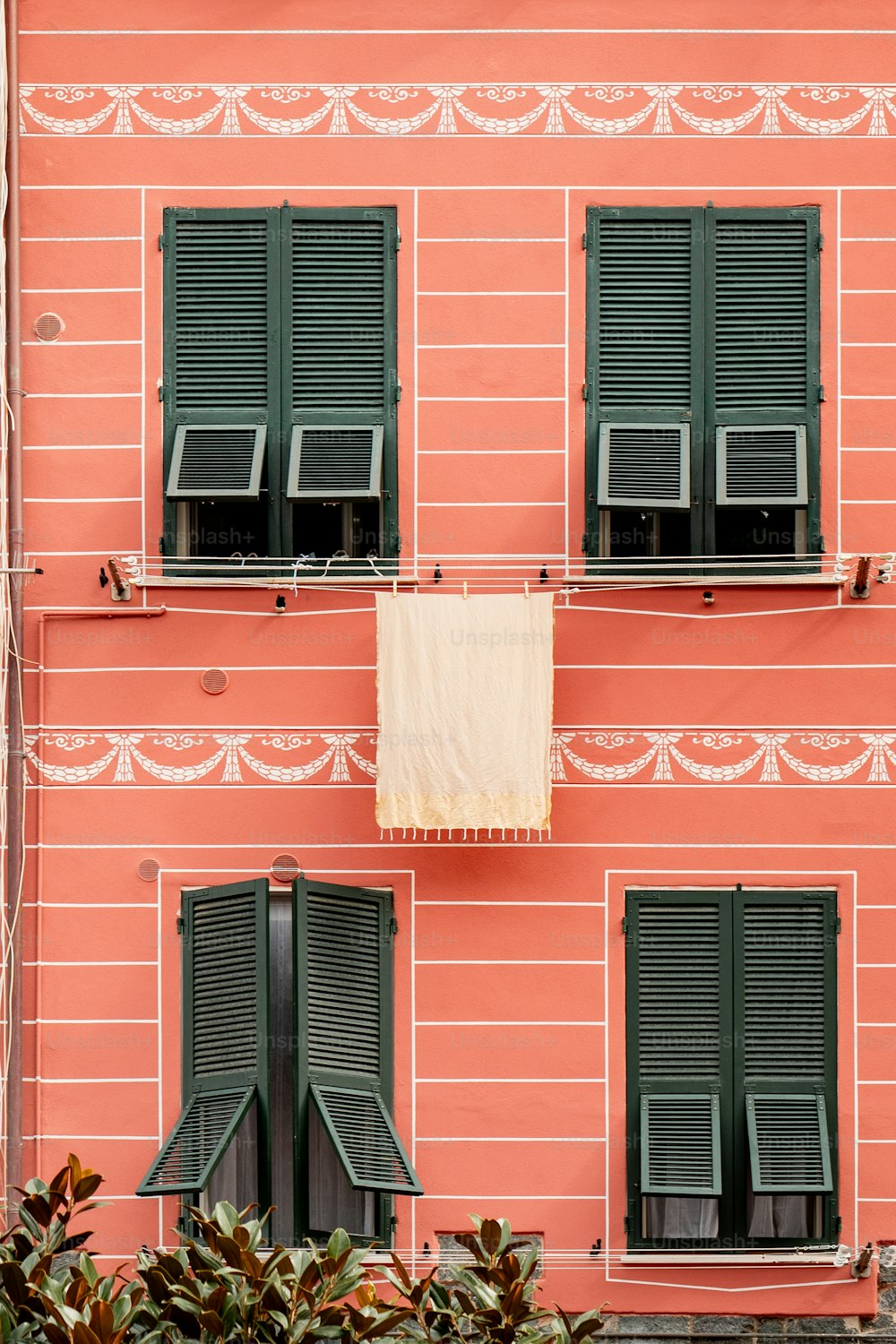 a pink building with green shutters and a towel hanging from the window