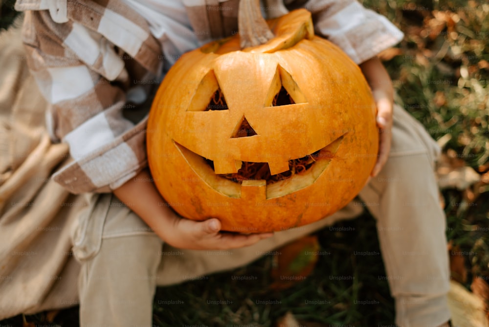 a young boy holding a carved pumpkin in his hands