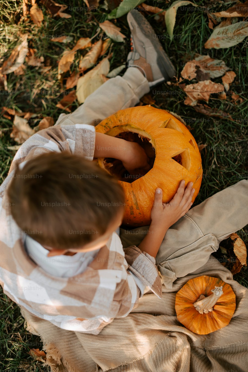 a young boy is carving a pumpkin in the grass