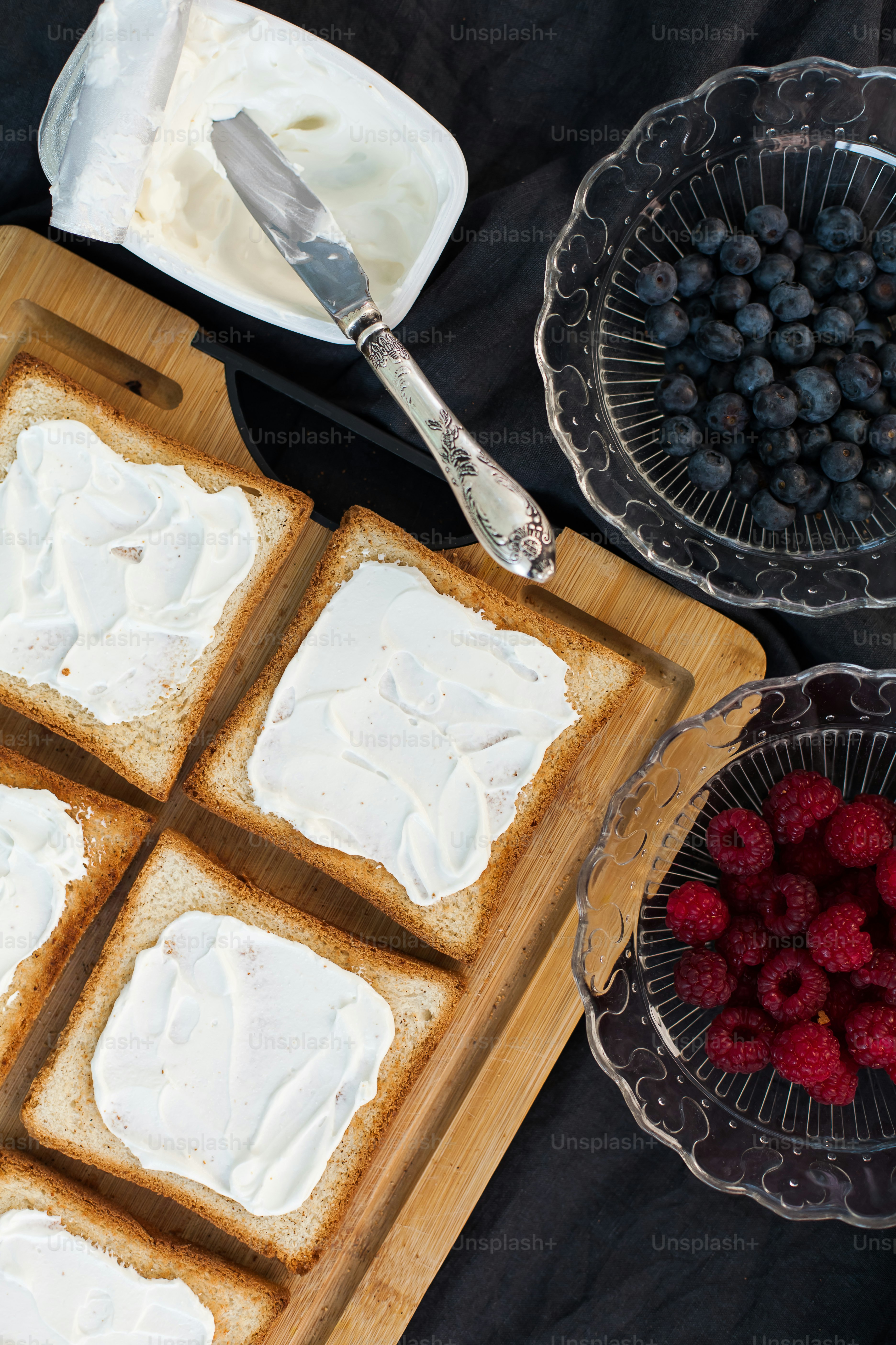 a wooden cutting board topped with white frosting and raspberries