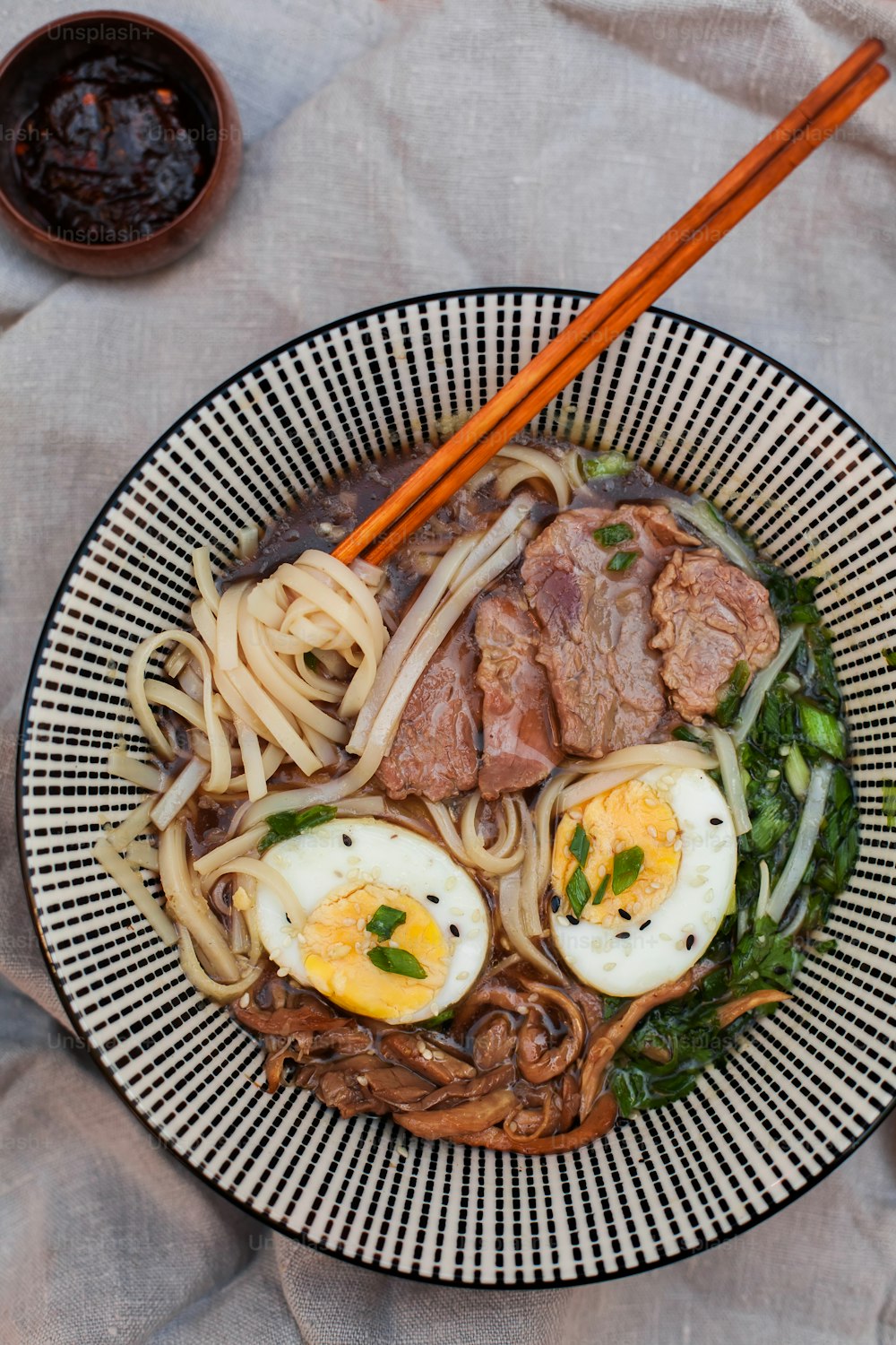 a bowl of noodles with meat and vegetables with chopsticks