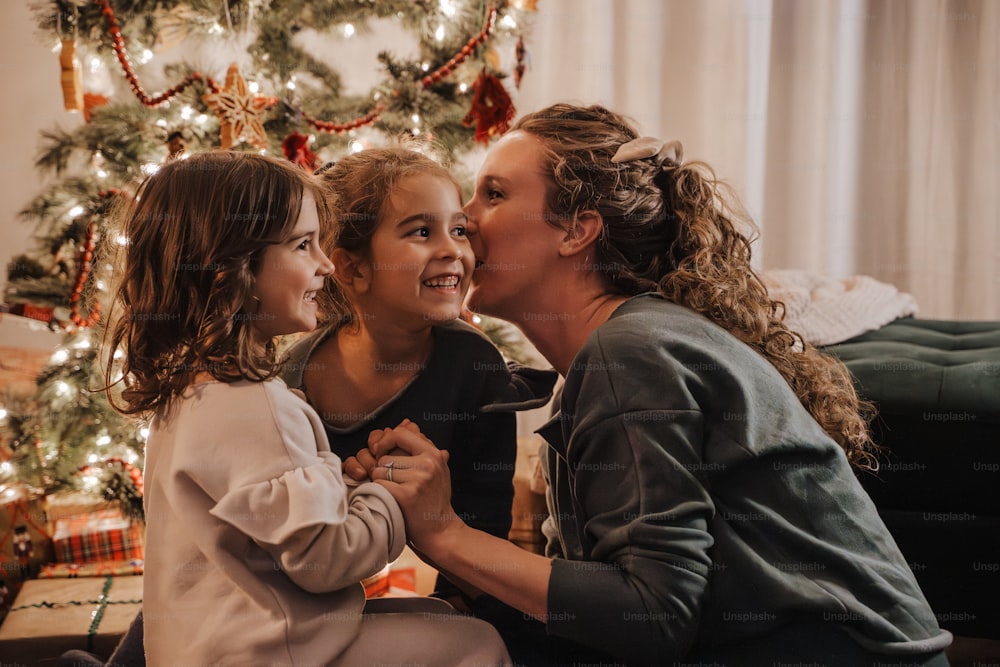 a woman and two young girls sitting next to a christmas tree
