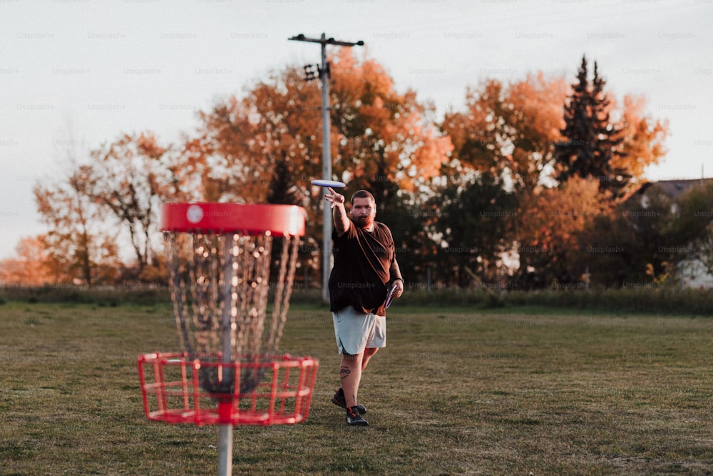 a man throwing a frisbee into a red frisbee golf basket