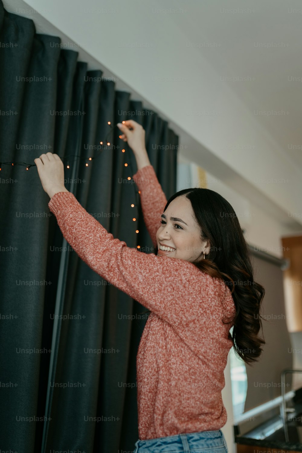 a woman standing next to a curtain holding a string of lights