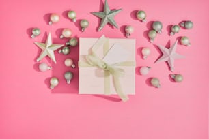 a gift box with a bow and ornaments on a pink background