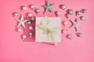 una confezione regalo con un fiocco e ornamenti su sfondo rosa