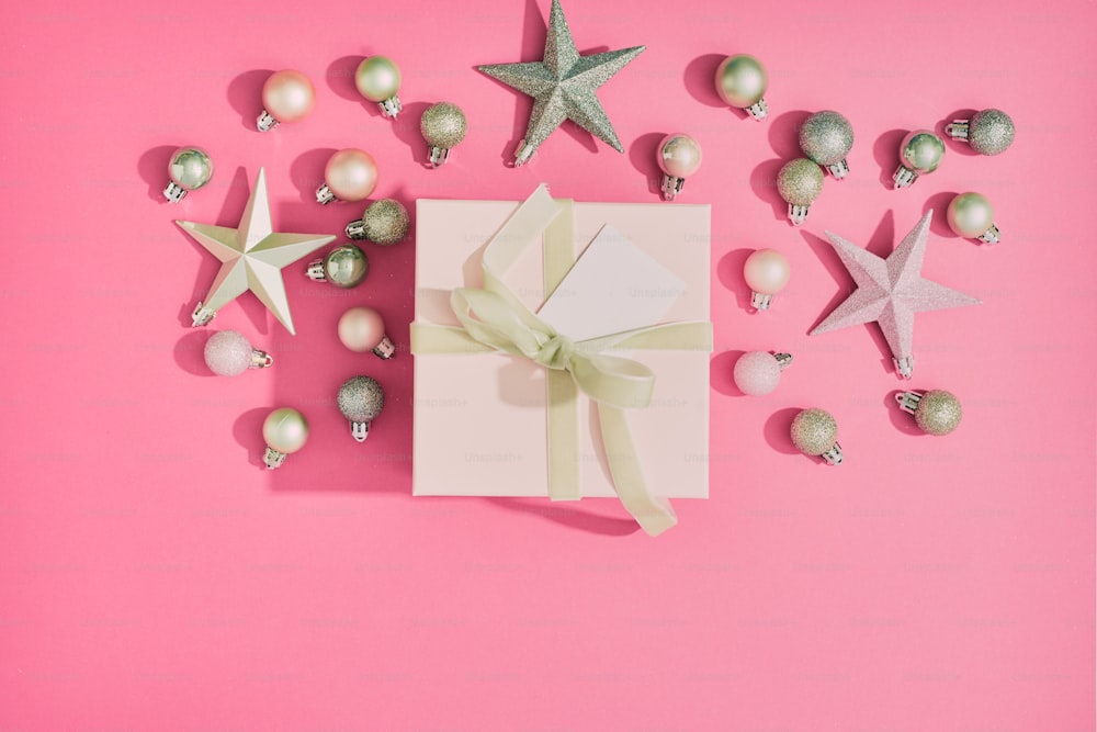 a gift box with a bow and ornaments on a pink background