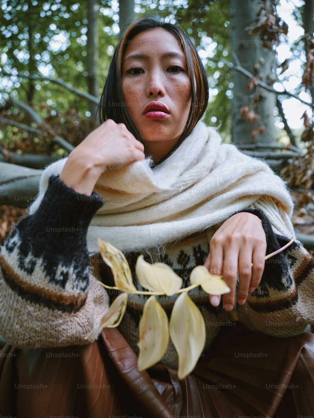 a woman sitting in the woods with a scarf around her neck