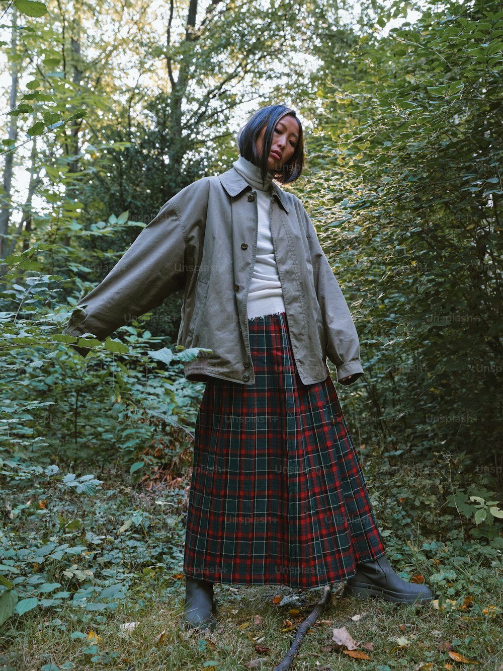 eine Frau, die im Wald steht und einen Rock und eine Jacke trägt