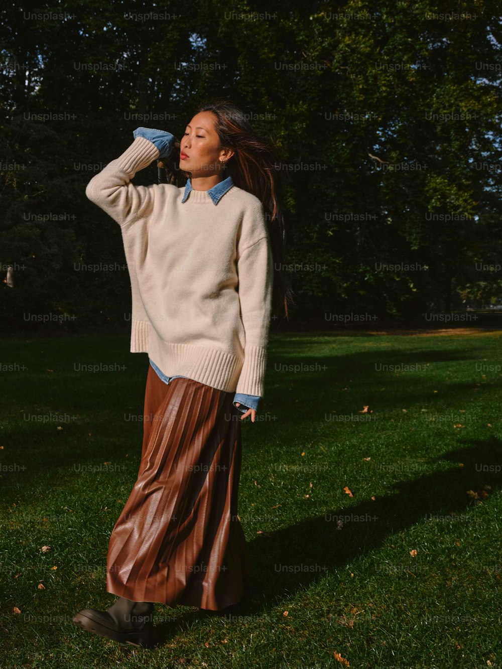 a woman standing in the grass wearing a sweater and pleated skirt