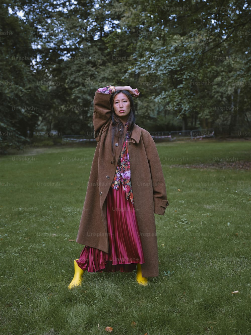a woman in a brown coat is standing in the grass