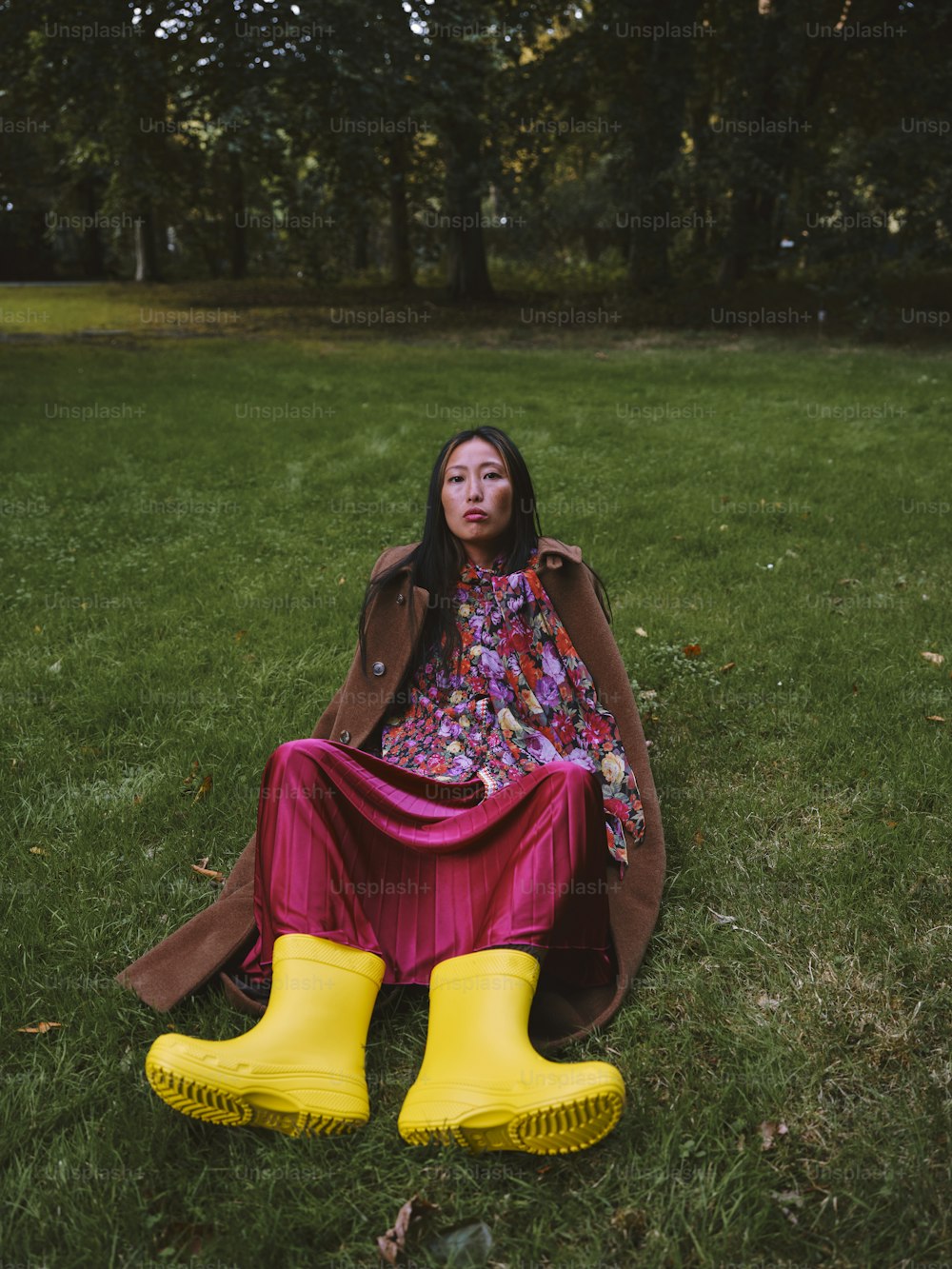 a woman sitting in the grass wearing yellow rain boots