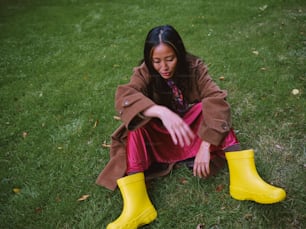 a woman sitting on the grass wearing yellow rain boots