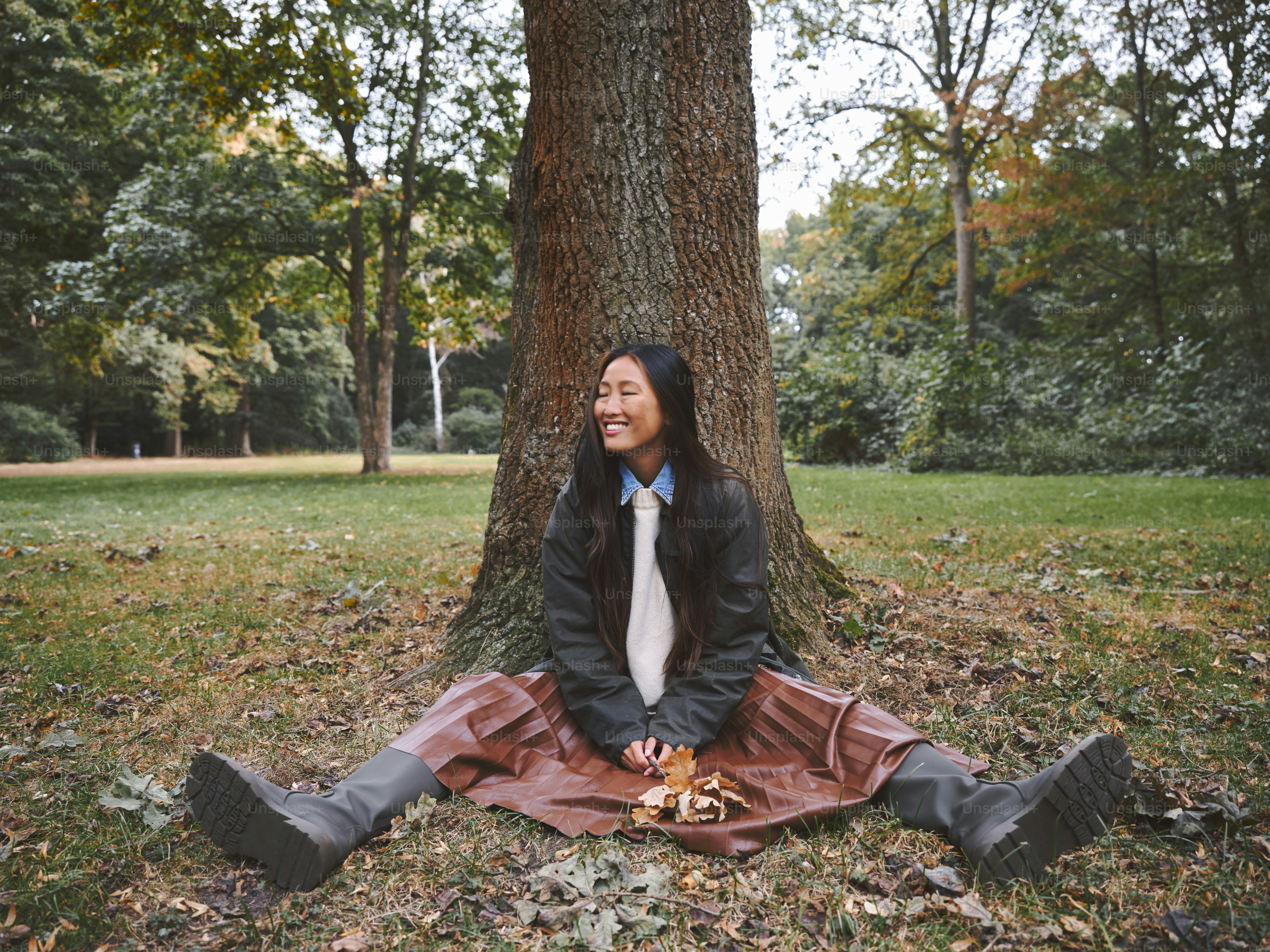 A woman sitting on the ground in front of a tree photo – Fall fashion ...