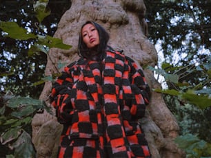 a woman standing in front of a tree wearing a black and red checkered coat