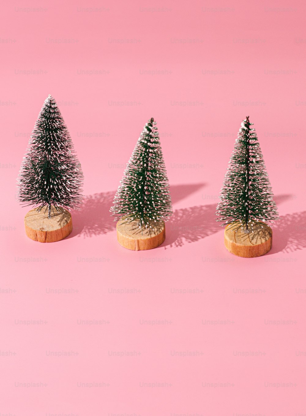 three small christmas trees sitting on top of a pink surface