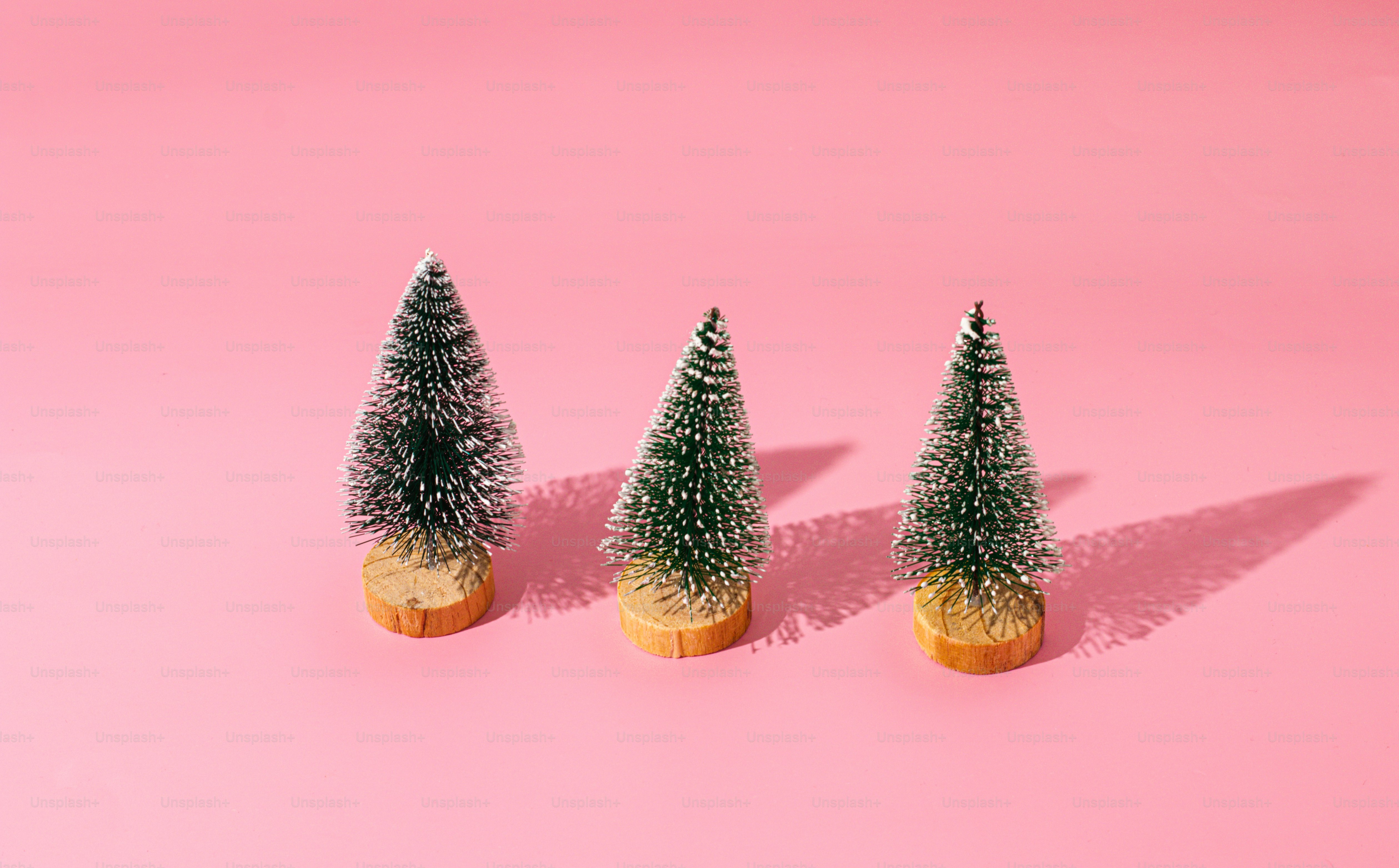 three small christmas trees sitting on top of a pink surface